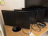 Three black computer monitors of similar size arranged side by side on a tabletop, with visible cables attached.