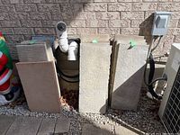 Photo showing multiple large rectangular patio stones stacked vertically against a brick wall, in shades of beige and gray.