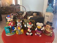 Wide shot of all piggy banks including four Chuck E. Cheese character banks, ceramic baby bottle, and two brown bear banks in a box