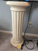 Close-up view of a round pillar-style plant stand with fluted column design and speckled light stone texture, showing size and texture details