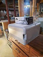 HP Color LaserJet CP1215 printer on wooden surface with MTC branded toner cartridge box on top. The photo shows the left side of the printer including power switch and vents.