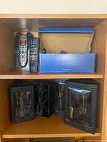 View of three TV remote controls and a blue box on a shelf
