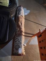 Rolled area rug placed on floor beside tires in basement, showing entire length and fringes.