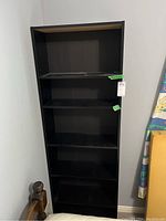 Front view of the black MDF shelving unit with four shelves placed against a white wall.