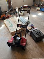 Red and black Toro Power Curve 1800 snow thrower with metal handlebar, placed on a garage floor surrounded by other items.