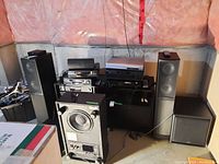 Overall view of electronics on black rack, two tall stand speakers and two cube subwoofers