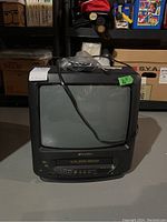 Sansui branded black 14-inch CRT television with built-in VHS VCR on front beneath screen, showing power cord draped over it.
