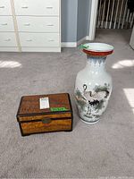 Photo showing both vase and wooden box side by side on carpeted floor with daylight.