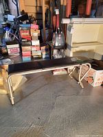Side angle view of the workout bench showing metal frame and vinyl padded top, placed indoors on concrete floor with boxes nearby.