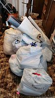 Multiple large bags filled with various textiles and fabric rolls on carpeted floor.