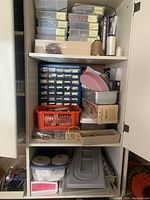 Closet shelf with multiple stacked plastic storage boxes and small clear drawer units filled with beading supplies and accessories.