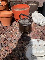 Image of assorted clay pots including terracotta pots, black metal watering can, and cement garden face plaques laying on garden rocks.