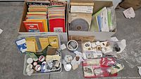 Two cardboard boxes of lapidary journals and polishing wheels with front tray of small containers holding mineral specimens