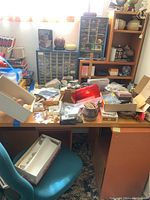 Workspace with teal office chair and tabletop covered in boxes, small drawers, minerals, shells, jewelry