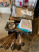 Open vintage fishing tackle box containing various fishing gear and wood handled items, with bamboo tiki torches beneath.