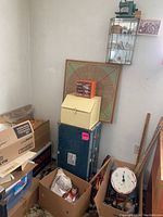 Glass wall-mounted curio cabinet hung on wall above blue trunk, containing porcelain figurines