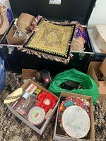 Open trunk with embroidered textile draped over edge and two open boxes of small items in front