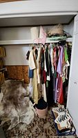 Wide view of closet showing hanging costumes, animal skin rug on floor, and hats on top shelf.