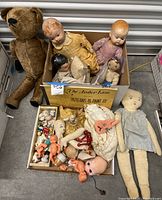 Lot of vintage dolls, doll parts, teddy bear, and pattern book in two boxes on floor
