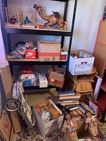 Full view of metal shelving unit with various boxes, dolls, and toys arranged on shelves and floor.