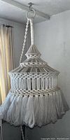 Vintage macrame light fixture hanging, showing detailed yarn weaving, braided top, and fringed bottom