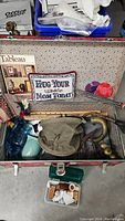 View inside the vintage trunk showing US canvas basket, bottles, pitcher, pillow, and horn.