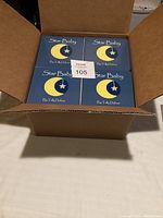 Open cardboard box showing the top view of 48 new kids books with blue cover titled Star Baby by Tally Dufour, depicting a crescent moon with stars.