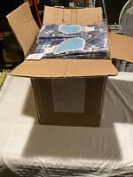 Open corrugated cardboard box on white cloth table showing multiple individually packaged bibs inside.