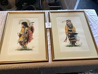 Two framed watercolour paintings by Ely Kish depicting Native American figures side-by-side on a table