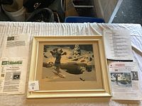 Framed art print placed on a white surface with related documents and information sheets visible beside it.