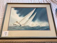 Framed watercolor painting showing sailing boats at sea, displayed on fabric surface.