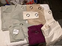 Overview of curtains in various colors and sizes, folded with metal grommets visible, showing the full assortment in the lot.