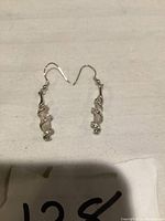 Pair of dangling earrings with clear cylinder wrapped by silver spiral with rhinestones on white fabric background.