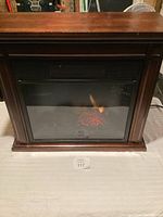 Electric heater with a wood frame and glass front showing artificial flames and embers