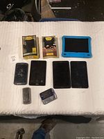 Photo showing laid out electronics and accessories including 4 smartphones, 2 phone cases, 1 tablet with blue case, and 2 small phones.