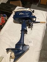 Full view of the outboard motor including the metal body, throttle lever with wooden handle, and propeller at the bottom.