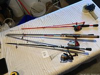 Overview of three fishing poles laid on a bed showing full length, various handles and reels attached.