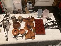 Overview of the lot on a white cloth including wooden carved art, wooden bowls, skull, metal racks, chess board, and pots.