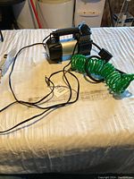 View of mini compressor with attached green coiled hose and power cord on table.