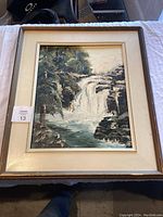 Full view of the framed oil painting showing the waterfall scene in forested rocky area.