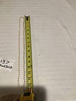 Pearl necklace laid flat next to tape measure showing length approx 14 inches.