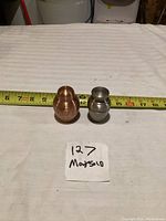 Two small pet urns on a white surface with measuring tape showing sizes approximately 3 to 4 inches tall.