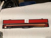 Pool cue placed in a closed black carrying case lined with red felt, showing the cue disassembled inside.