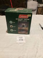 Front view of Coleman Ultralight Propane Stove 10,000 BTU box on a table with auction lot number in front.