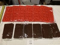 Lot of silicone molds arranged on table showing red molds with single alphabet letters each and brown molds with two characters per mold; all packaged new.