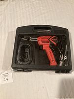Weller soldering iron inside molded black carrying case, showing red soldering gun with power cord attached.