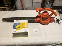 Black+Decker orange electric leaf blower with handle and power cord next to the 3M TaperFit 2 earplugs retail box.