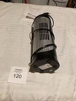 Side view of the black tower fan with power cord wrapped around, placed on a white surface.