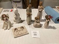 Photo of collection of Willow Tree figurines and one white ceramic rabbit on a white surface, showing front and side views of each piece.