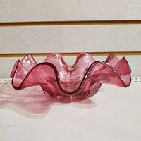 Side view of cranberry glass bowl showing ruffled edge and color depth.
